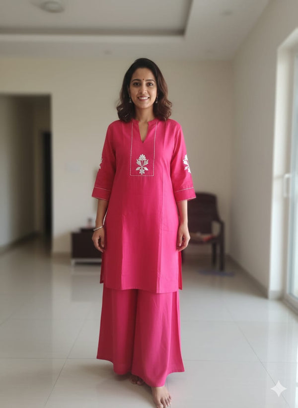 Woman wearing a pink traditional outfit in a room with white walls and tiled floor.