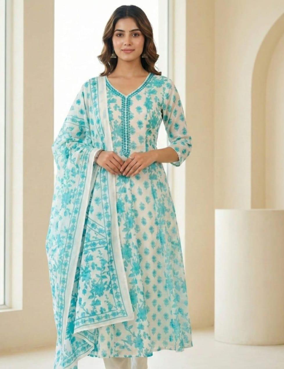A woman modeling a light blue and white printed traditional kurta set with a matching dupatta in a softly lit indoor setting.