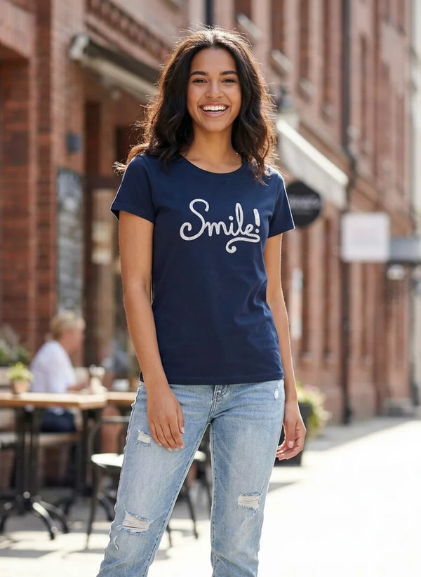 Woman wearing a navy blue t-shirt with 'Smile!' text, standing on a street.