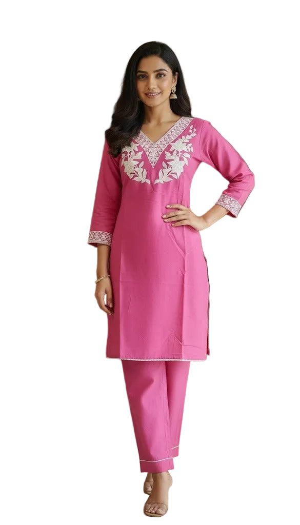 Woman wearing a pink traditional outfit with white embroidery in a room.