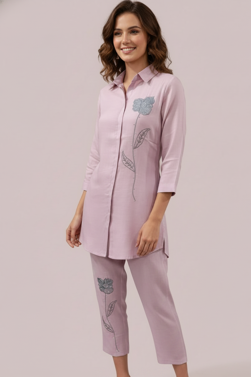Woman wearing a pink outfit with embroidered designs on a plain background