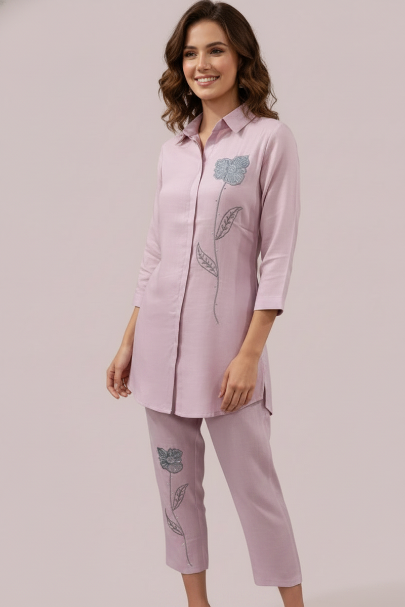 Woman wearing a pink outfit with embroidered designs on a plain background